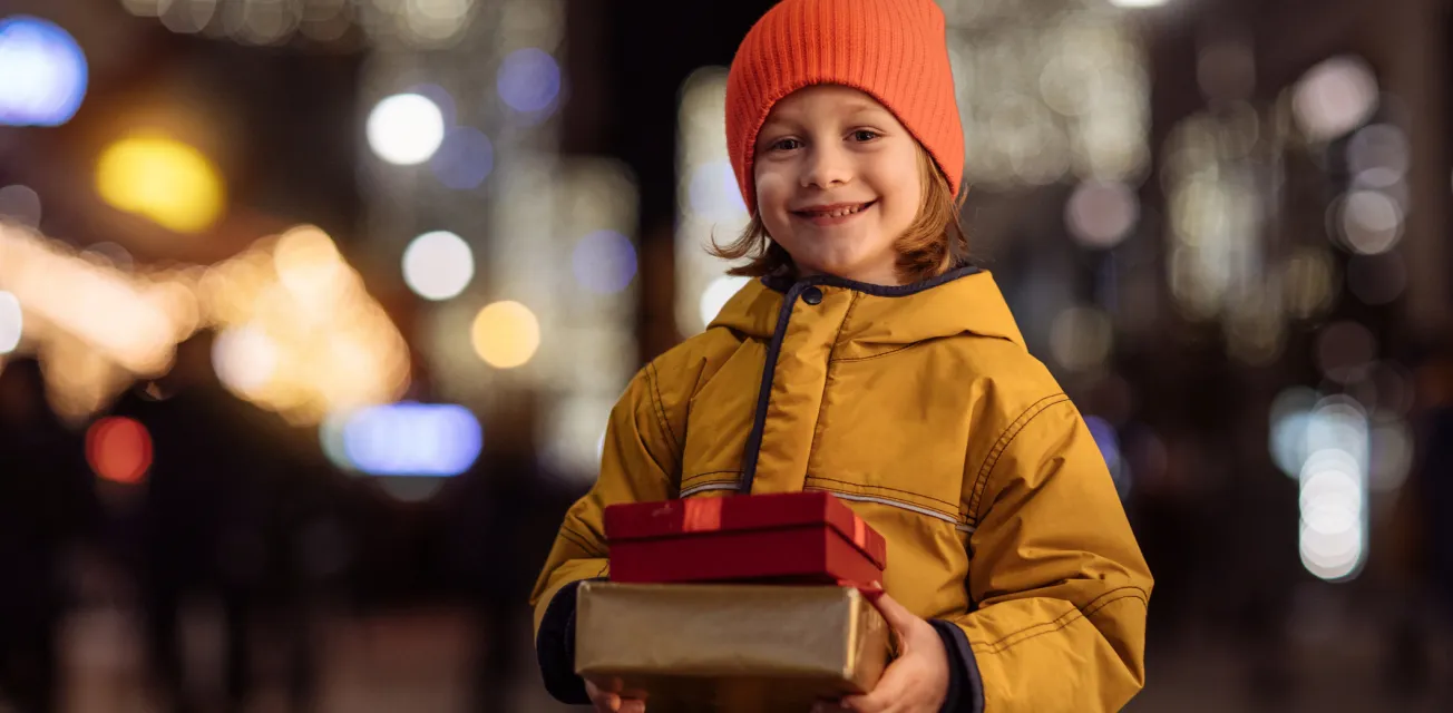 Leende barn i ytterkläder med två paket i händerna.