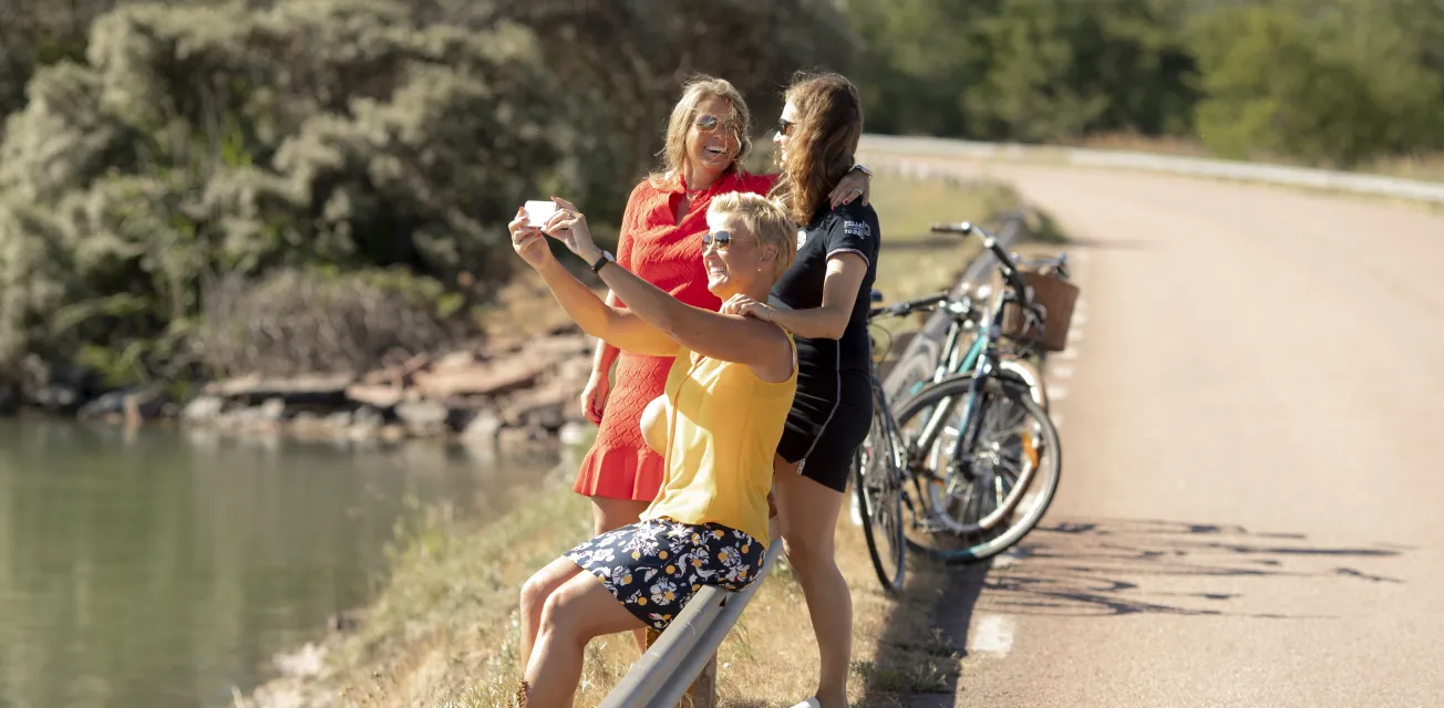 Kvinnor med cyklar som stannat vid brobank för fotografering.